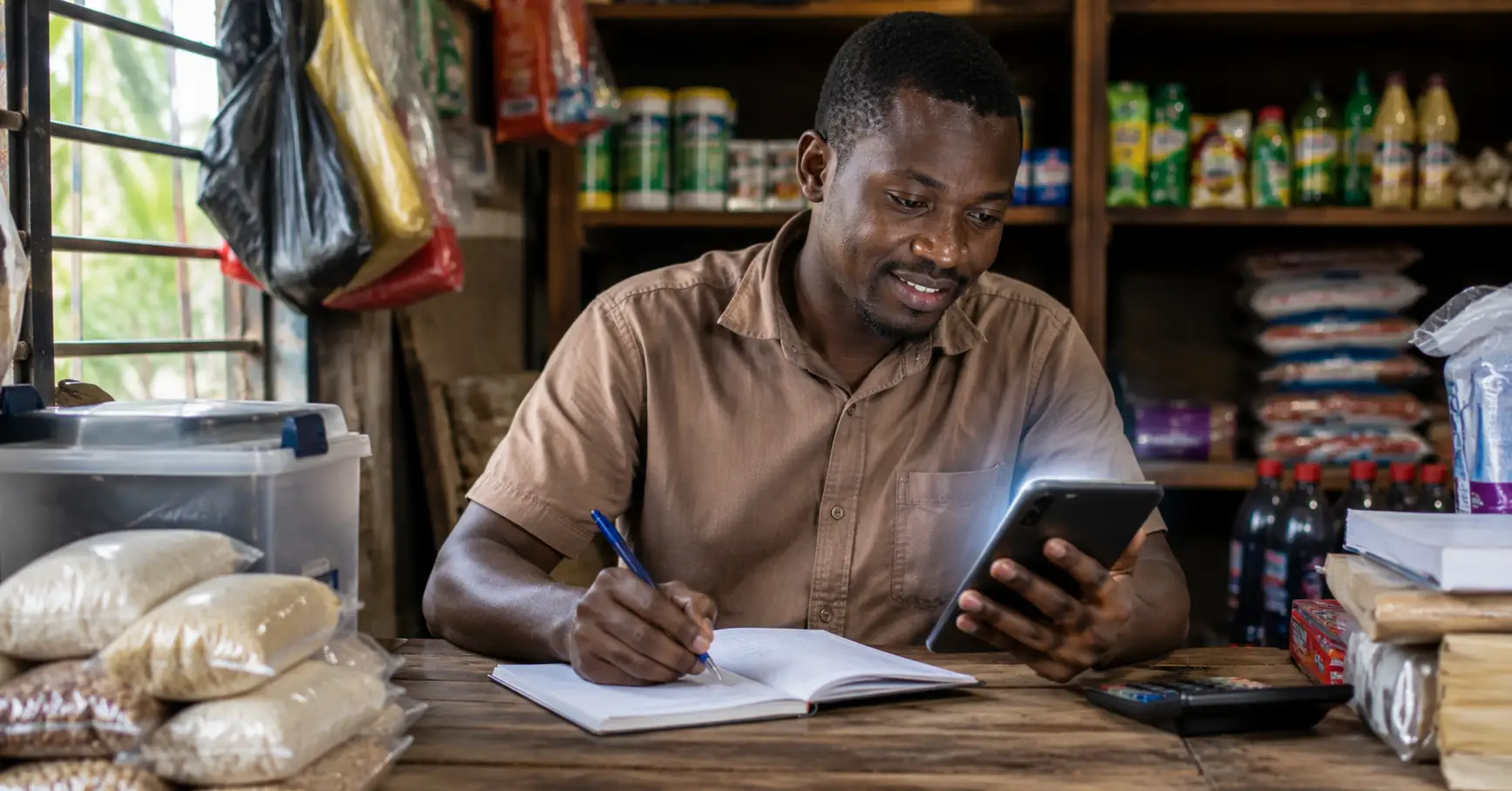 Ghanaian shop owner using AI on smartphone while managing inventory and records